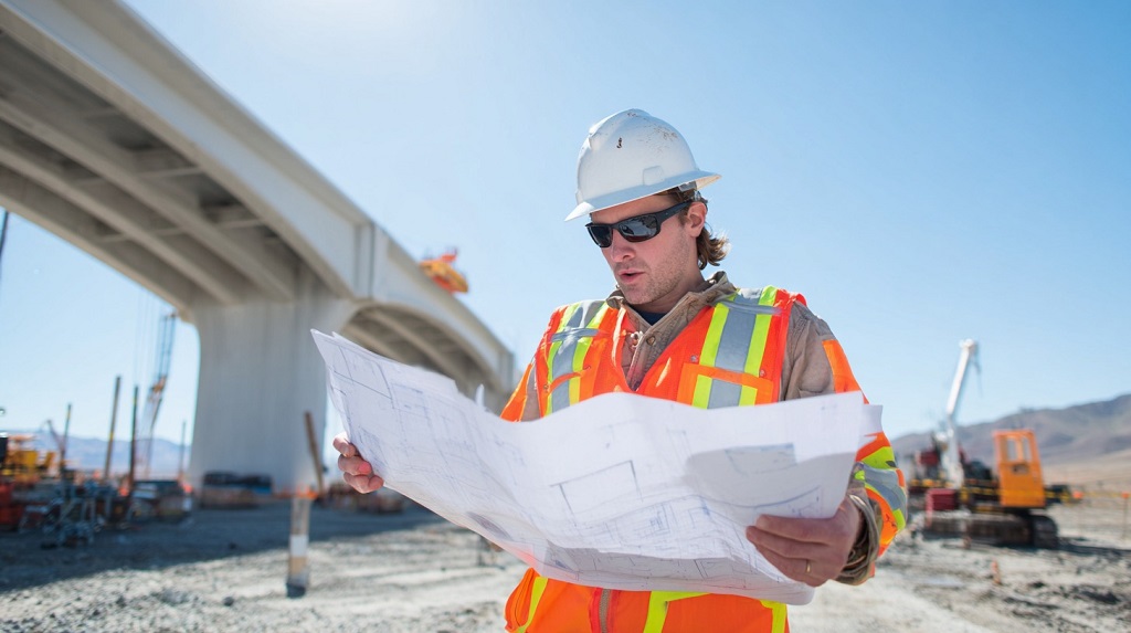 Civil engineer in a reflective vest reviewing bridge construction plans at a job site