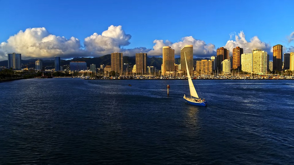 Sailboat in front of Honolulu’s skyline with tropical towers and ocean reflections